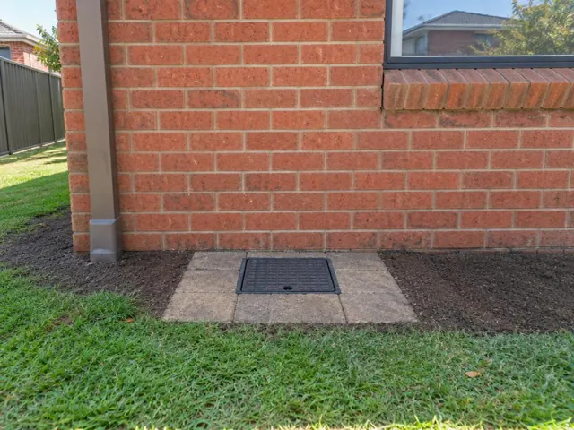 Square capped access cover set in paving beside a brick house wall in Wakeley
